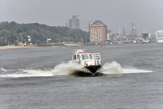 A speedboat cruises quickly through the harbour water and leaves waves in its wake, Hamburg,