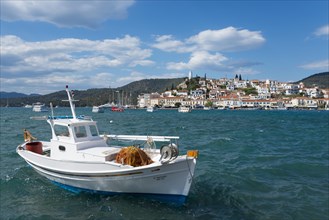 A fishing boat on the sea in front of a picturesque coastal town under a partly cloudy blue sky,