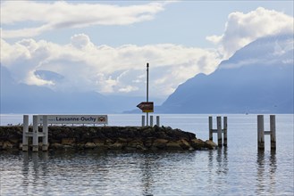 Headland with sign for the harbour of Lausanne-Ouchy and Duckdalben in Lake Geneva with fog-covered