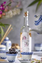 Pouring tea, Asian tea set with blue patterns, a bottle of China plum wine in the background, dried