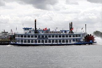 An antique paddle steamer named 'Louisiana Star' sailing on the water against a cloudy sky,