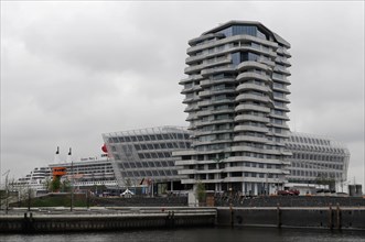 Marco Polo Tower, cruise ship behind a modern building facade on a cloudy day, Hamburg, Hanseatic
