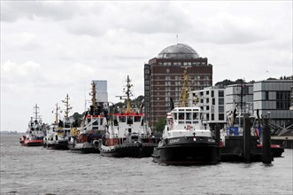 A row of tug boats at the quay in an urban harbour under a grey sky, Hamburg, Hanseatic City of