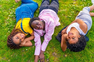 Three young female african friends enjoying spring lying on the green grass of a park