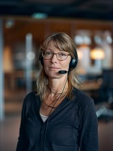 Mature professional woman with headset in a calm office setting with neutral colors, AI generated