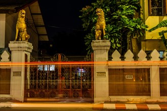 Long exposure captures the light trails at a temple gate with guarding statues, in Chiang Mai,