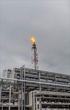 Fire atop a flare stack within a sprawling industrial facility under an overcast sky, in Ulsan,
