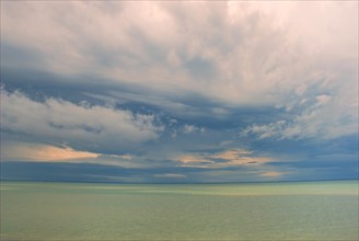 A serene seascape with a horizon dividing a cloudy sky and calm green-blue water