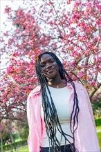 Vertical portrait of a beauty african woman smiling at camera next to flowering tree with pink