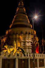 A temple's warm tones are highlighted by a spotlight against the night sky, in Chiang Mai,