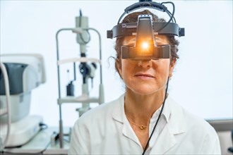 Portrait frontal view of female ophthalmologist using the light of a head torch of a retinoscope