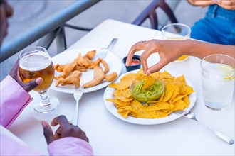 Hands of a woman dipping a nacho into guacamole sauce enjoying meal with friends in a restaurant