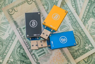 Blue and yellow USB hardware wallets with Bitcoin logos arranged on dollar bills, in South Korea