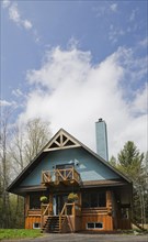 Post and beam cottage style hybrid log home facade with blue clapboard trim and timber elements in