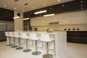 Quartz countertop island with white leather and stainless steel barsrools in spacious kitchen