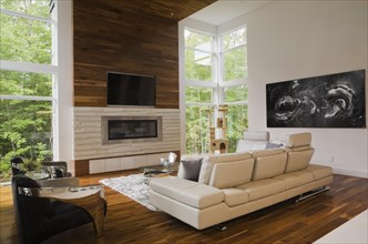 Living room with creamy beige colored L-shaped leather sofa and gas fireplace inside luxurious