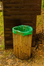 A green-topped trash can with a bamboo exterior stands beside a wooden board, in South Korea