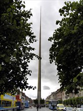 A slender monument rises between green trees under a cloudy sky Ireland's capital Dublin