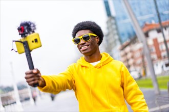 African young influencer broadcasting live in the city using a mobile attached on a tripod and