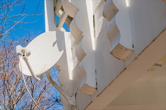 Satellite dish mounted on white architectural structure with clear blue sky in the background, in
