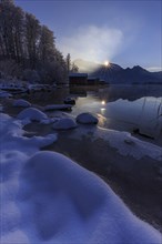 Evening mood at mountain lake in front of mountains, boat huts, shore, winter, snow, reflection,