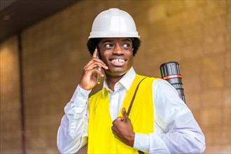 Portrait of a happy young african architect wearing protective work clothes and helmet talking to