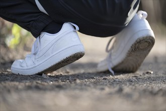 White trainers of an athletically dressed boy, crouched posture, on a gravel path, sole visible, at