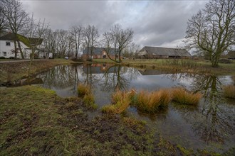 Manor house, horse stable and barn from 1920, in front the extinguishing pond, in cloudy weather,
