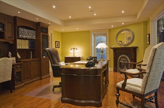 Wooden desk, high back chairs and wall unit in basement home office inside elegant style home,