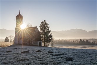 Chapel at sunrise in front of mountains, backlight, sunbeams, hoarfrost, winter, Sankt