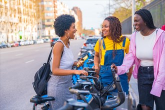 Three african young happy friends renting public bike using phone in the city