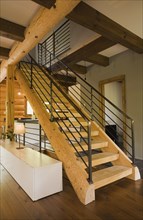 Wooden log stairs with black wrought iron railings and long cabinet table inside contemporary style