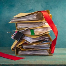 A large pile of files, bound with a red ribbon, on a wooden table in front of a blue wall,