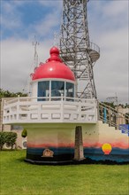 A red lighthouse replica in front of a communication tower under a clear sky, in Ulsan, South