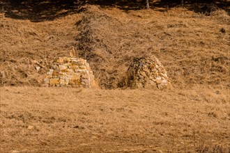 Two pyramid shaped rock structures in field of brown grass at foot of hillside in Boeun, South