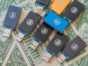 Multiple USB hardware wallets with Bitcoin logos scattered on US dollar bills, in South Korea