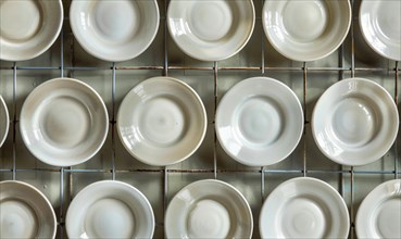 Neatly arranged white ceramic plates in a grid pattern, showing uniformity and cleanliness AI