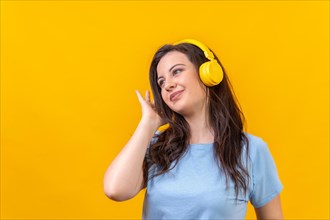 Studio portrait with yellow background of a cute woman listening to music with wireless headphones