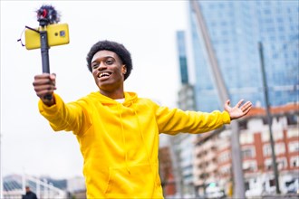 Happy african young streamer smiling at camera while broadcasting using phone in the city