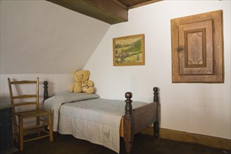Antique wooden weaved seat chair and single four-poster bed in bedroom on upstairs floor inside old