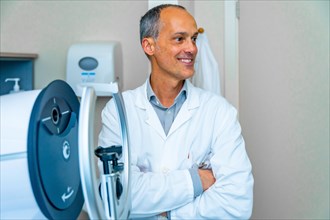 Proud mature male ophthalmologist looking distracted next to an innovative laser machine in a
