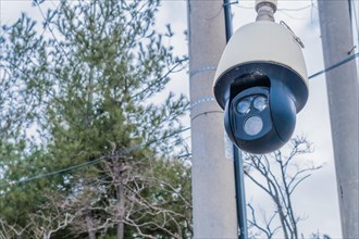 Closeup of round black surveillance camera in front of utility poles with blurred background in