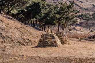 Two pyramid shaped rock structures in field of brown grass at foot of hillside in Boeun, South