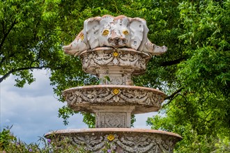 Ornate weathered fountain adorned with flowers and surrounded by green trees, in Chiang Mai,