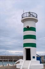 A lighthouse with green stripes stands against an overcast sky near the ocean, in Ulsan, South