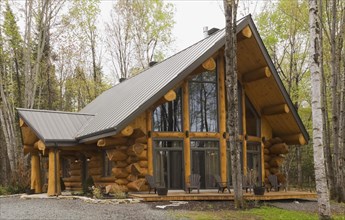 Luxurious Scandinavian style log home facade with large panoramic windows in spring, Quebec,