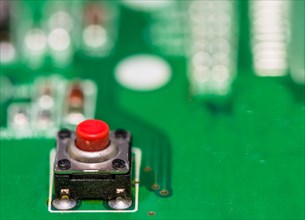 Red button on green circuit board with other components blurred out in background