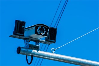 Closeup of closed circuit camera mounted on metal pole against light blue sky in background in