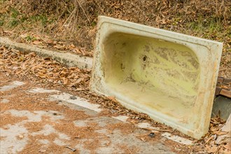 An old, dirty bathtub left upside down beside a path with leaves, in South Korea