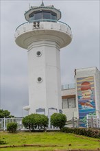 White lighthouse with a beacon on top, surrounded by trees and a wall mural, in Ulsan, South Korea,